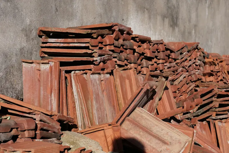 Tuiles en terre cuite déposées et empilées contre un mur avant une réfection de toiture