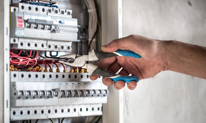 Électricien serrant un conducteur à la pince dans un tableau électrique équipé de disjoncteurs modulaires