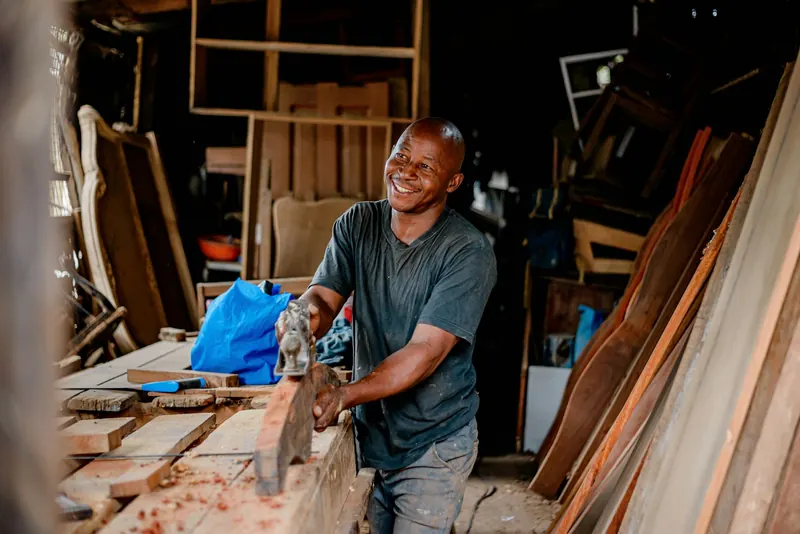 Menuisier souriant travaillant une planche dans son atelier, entouré de pièces de bois