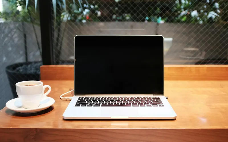 Ordinateur portable ouvert et tasse de café posés sur un bureau en bois