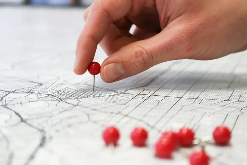 Main plantant une épingle rouge sur un plan de ville imprimé