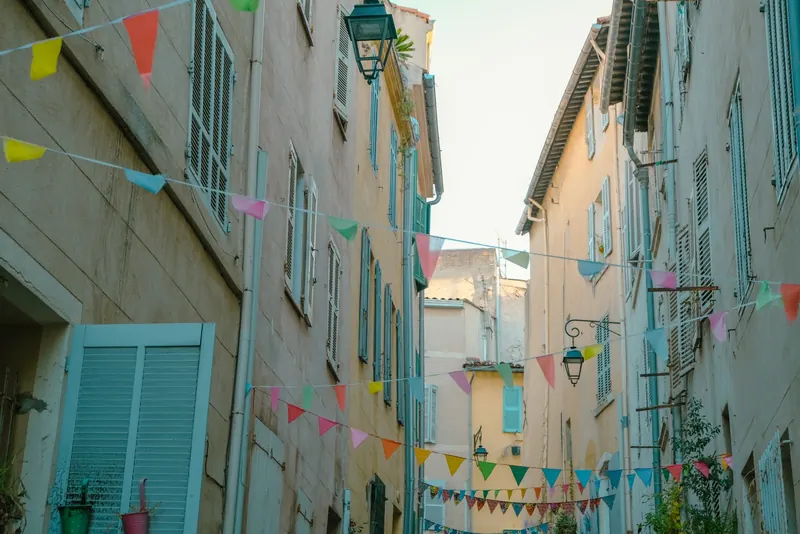 Ruelle étroite bordée de façades aux volets bleus, traversée de guirlandes de fanions