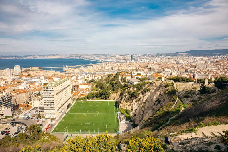 Ville côtière vue depuis une colline, avec un terrain de football au premier plan et la mer au fond